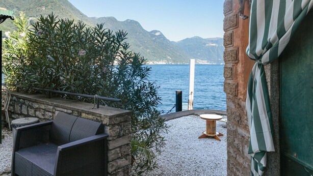 Eine Terrasse mit Korbstuhl, einem kleinen runden Tisch und Blick auf das Meer und die Berge.