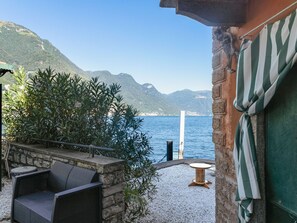 Eine Terrasse mit Korbstuhl, einem kleinen runden Tisch und Blick auf das Meer und die Berge.