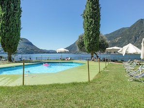 Une piscine entourée de montagnes, avec des chaises longues et des parasols, sous un ciel dégagé.