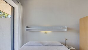 Ein schlicht eingerichtetes Hotelzimmer mit einem großen Bett, einem Nachttisch mit Telefon und einem wandmontierten Regal.