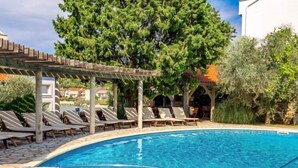 A swimming pool with lounge chairs and a pergola, surrounded by trees and a building in the background. - Apartment Mare 3 by Interhome (Rab/Kampor)