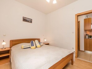 Ein Schlafzimmer mit einem hölzernen Bett, zwei Nachttischlampen, einem Nachttisch, einem Bild an der Wand und einer Holztür, die in eine Küchenzeile führt.