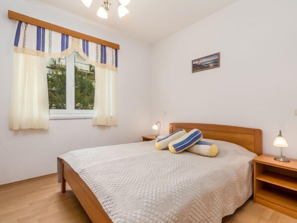 A bedroom with a bed, two bedside tables, a window with curtains, and a painting on the wall.