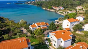 A coastal residential area with houses featuring red-tiled roofs, surrounded by greenery and a clear view of the sea. - Tomislav 1 by Interhome (Rab/Kampor)