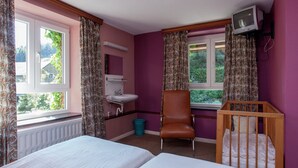 Een kamer met twee bedden, een stoel, een wieg, een televisie, een wastafel en gordijnen.