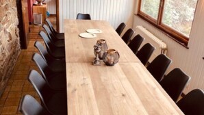 Een lange houten tafel met zwarte stoelen, een vaas en twee borden.