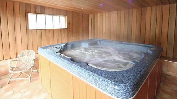 Een hottub in een houten kamer met een raam en een stoel.