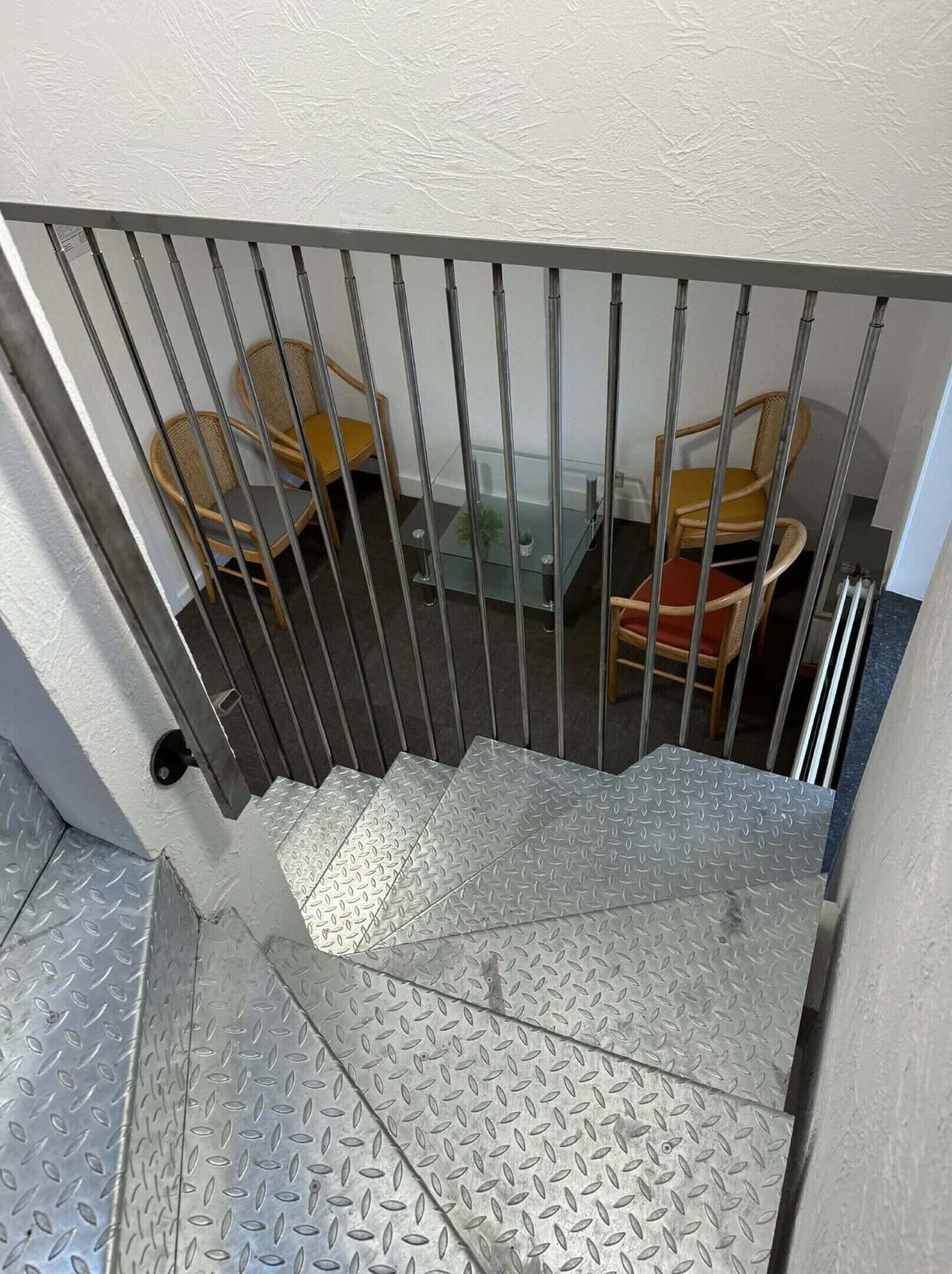 Una escalera metálica con superficie de rejilla que lleva a una habitación con sillas de mimbre y una mesa de cristal.