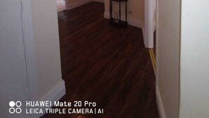 A hallway with a dark wooden floor, a white door on the left, a red pendant light, and a small table with a vase of flowers. - City center 2 bed apartment (Londonderry)