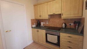 A compact kitchen with wooden cabinets, a built-in oven, and a countertop with various appliances. - City center 2 bed apartment (Londonderry)