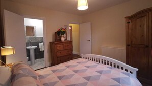 A bedroom with a bed, dresser, and a bathroom visible through an open door. - City center 2 bed apartment (Londonderry)