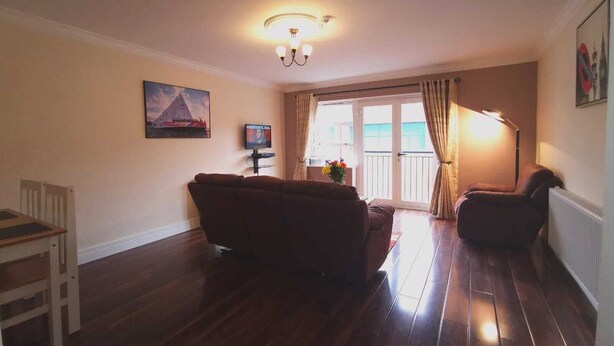A living room with a sofa, a television, a painting, and a window with curtains. - City center 2 bed apartment (Londonderry)