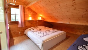 A cozy attic bedroom with a wooden sloped ceiling, a bed with cartoon character bedding, a window with a curtain, and two wall-mounted lights. - Chalet in Ardennes With Sauna & Garden (Waimes)