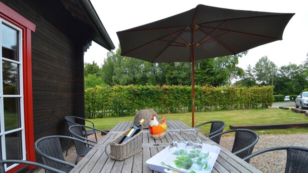 An outdoor patio with a wooden table, wicker chairs, a large umbrella, and a bottle of champagne. - Chalet in Ardennes With Sauna & Garden (Waimes)