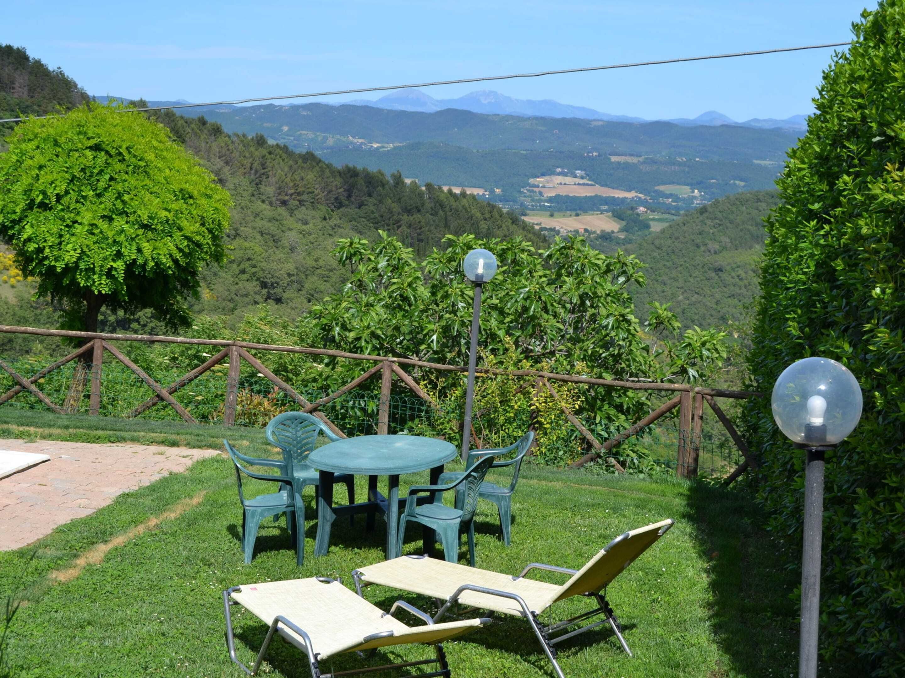 An outdoor seating area with a table and chairs, surrounded by a wooden fence, overlooking a mountainous landscape.