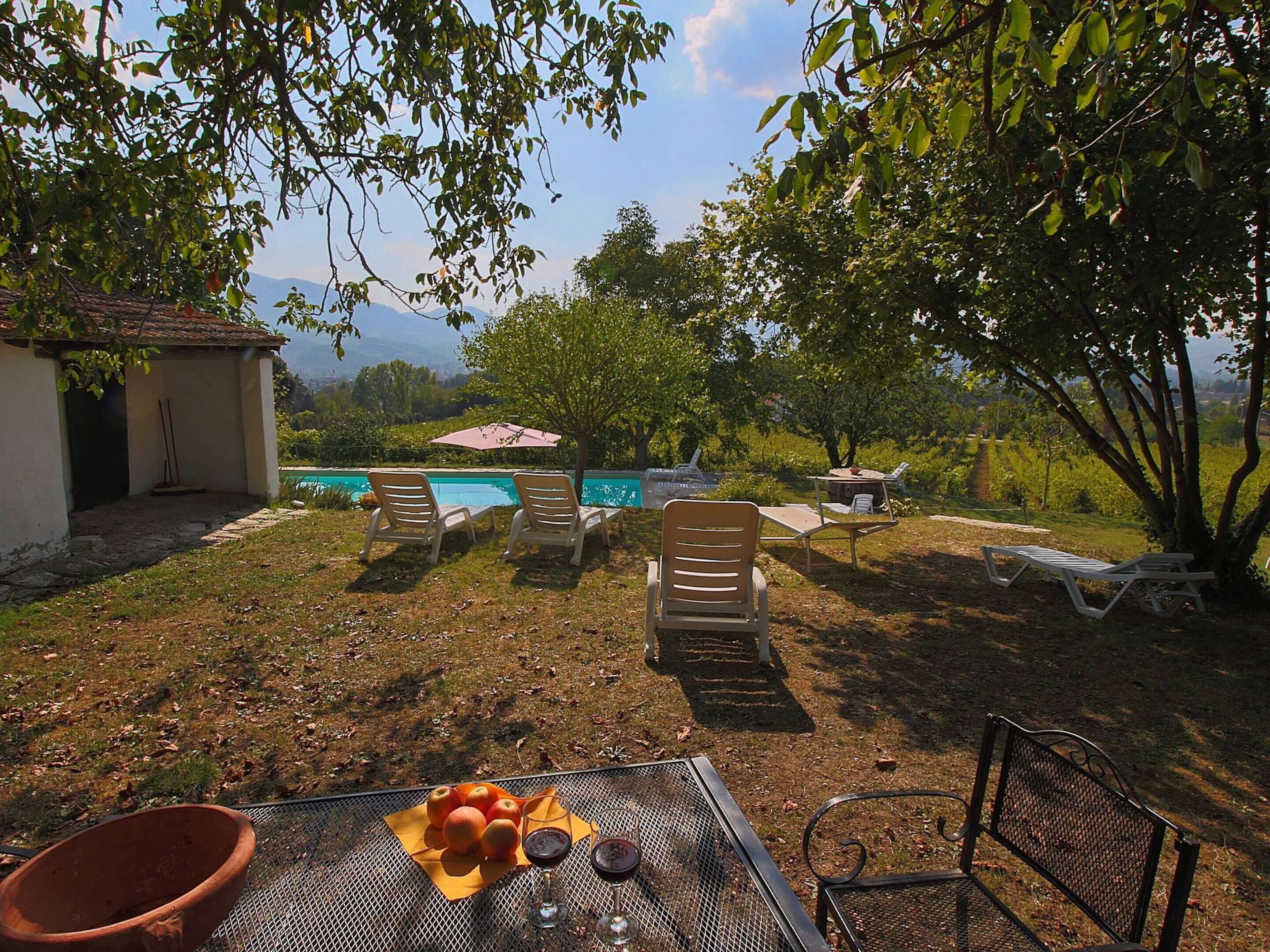 A poolside area with lounge chairs, a table with fruit and drinks, and a view of mountains.