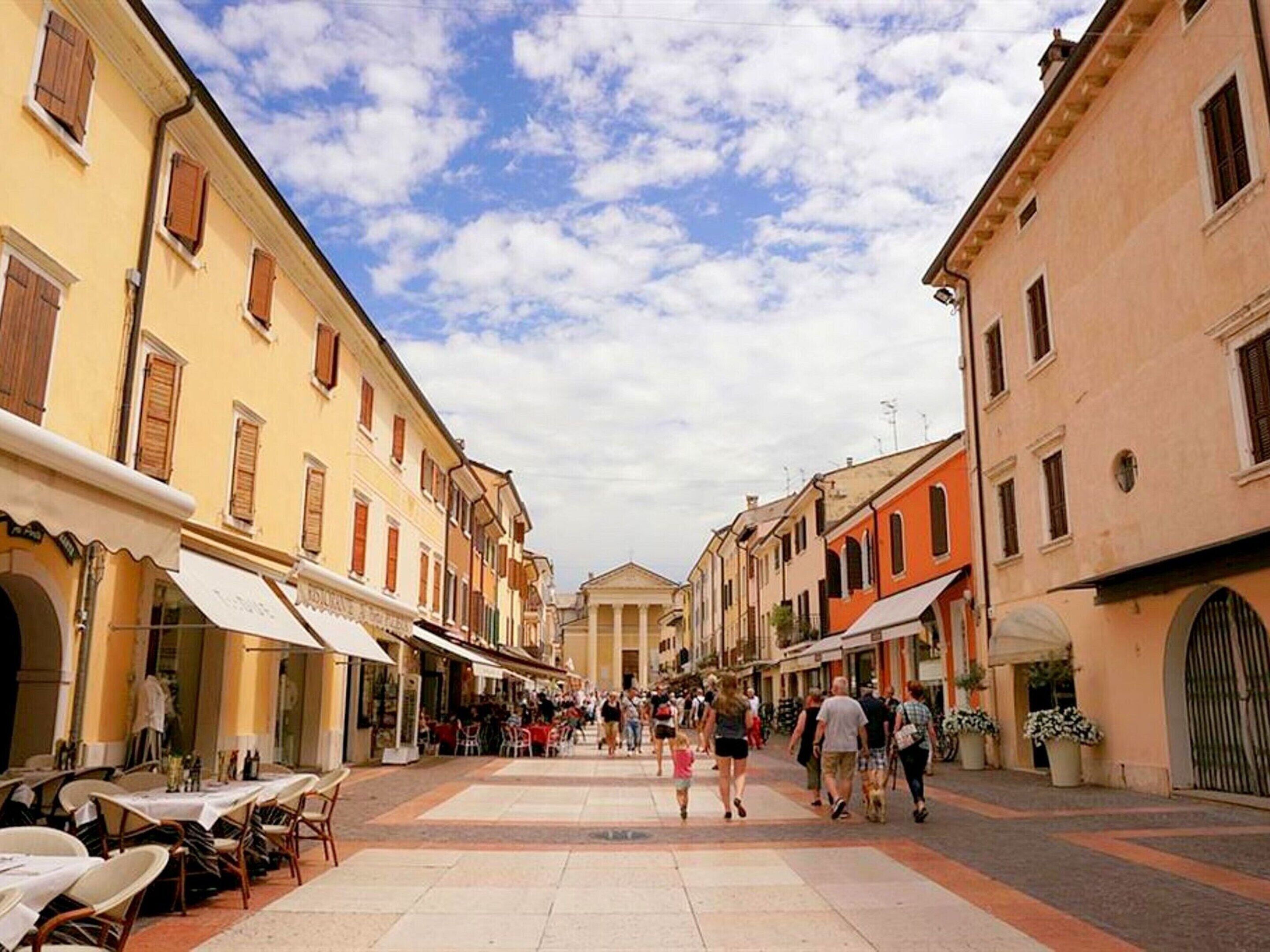 A pedestrian street lined with cafes and shops, with people walking and dining.
