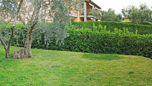 A residential building with a stone facade, a balcony, and a well-maintained garden with hedges and a tree. - Great and Colourful Apartment Near Bardolino (Bardolino)