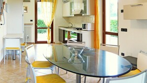 A modern kitchen with a dining area, featuring a glass table and chairs, a built-in microwave, and a view of greenery outside. - Great and Colourful Apartment Near Bardolino (Bardolino)