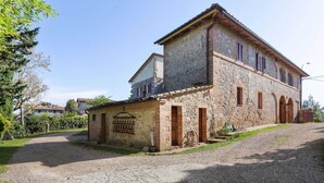 Un edificio de piedra con un camino de grava, una pequeña construcción adosada y una verja metálica.