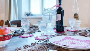 Uma mesa de jantar posta com copos de vidro transparente, uma garrafa de vinho e um abajur antigo.