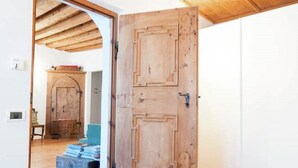 Um quarto com porta de madeira, uma cama, uma mesinha e uma cadeira.