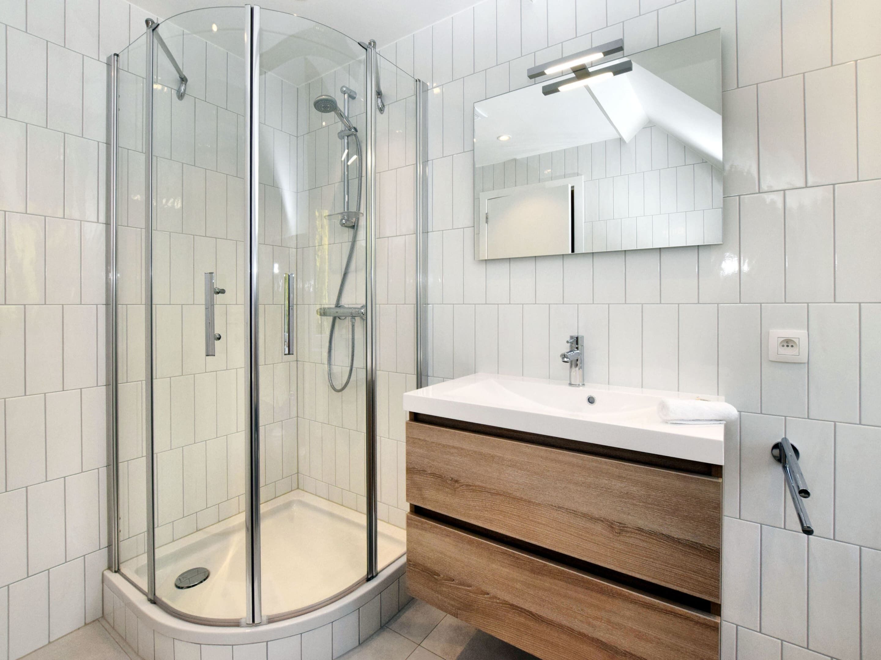 A modern bathroom with a glass-enclosed shower, a white sink, and wooden vanity drawers.