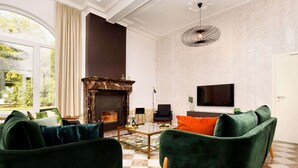 A living room with a fireplace, green velvet sofas, a television, and a large window with curtains. - Opulent Holiday Home in Spa with Sauna, Hot Tub, Playroom (Spa)