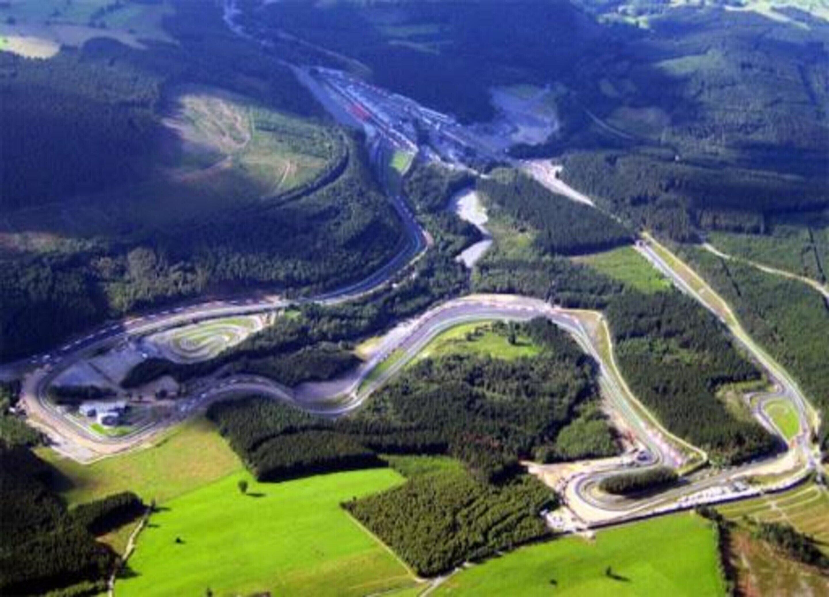 An aerial view of a winding road through a forested area with green fields.