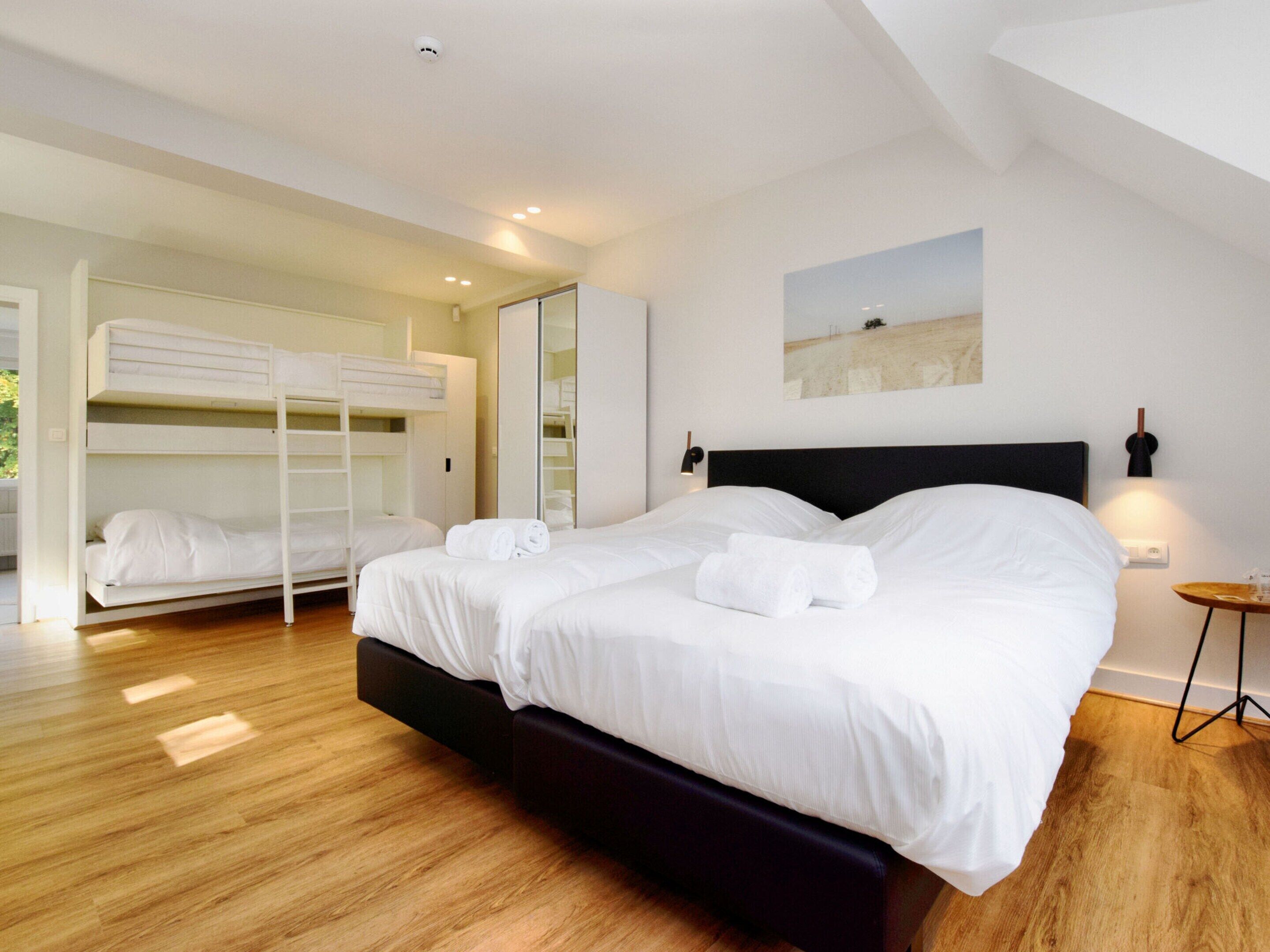 A modern hotel room with a large bed, a bunk bed, wooden flooring, and a painting on the wall.