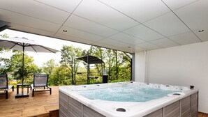 A hot tub on a wooden deck with a pergola and chairs, surrounded by trees. - Opulent Holiday Home in Spa with Sauna, Hot Tub, Playroom (Spa)