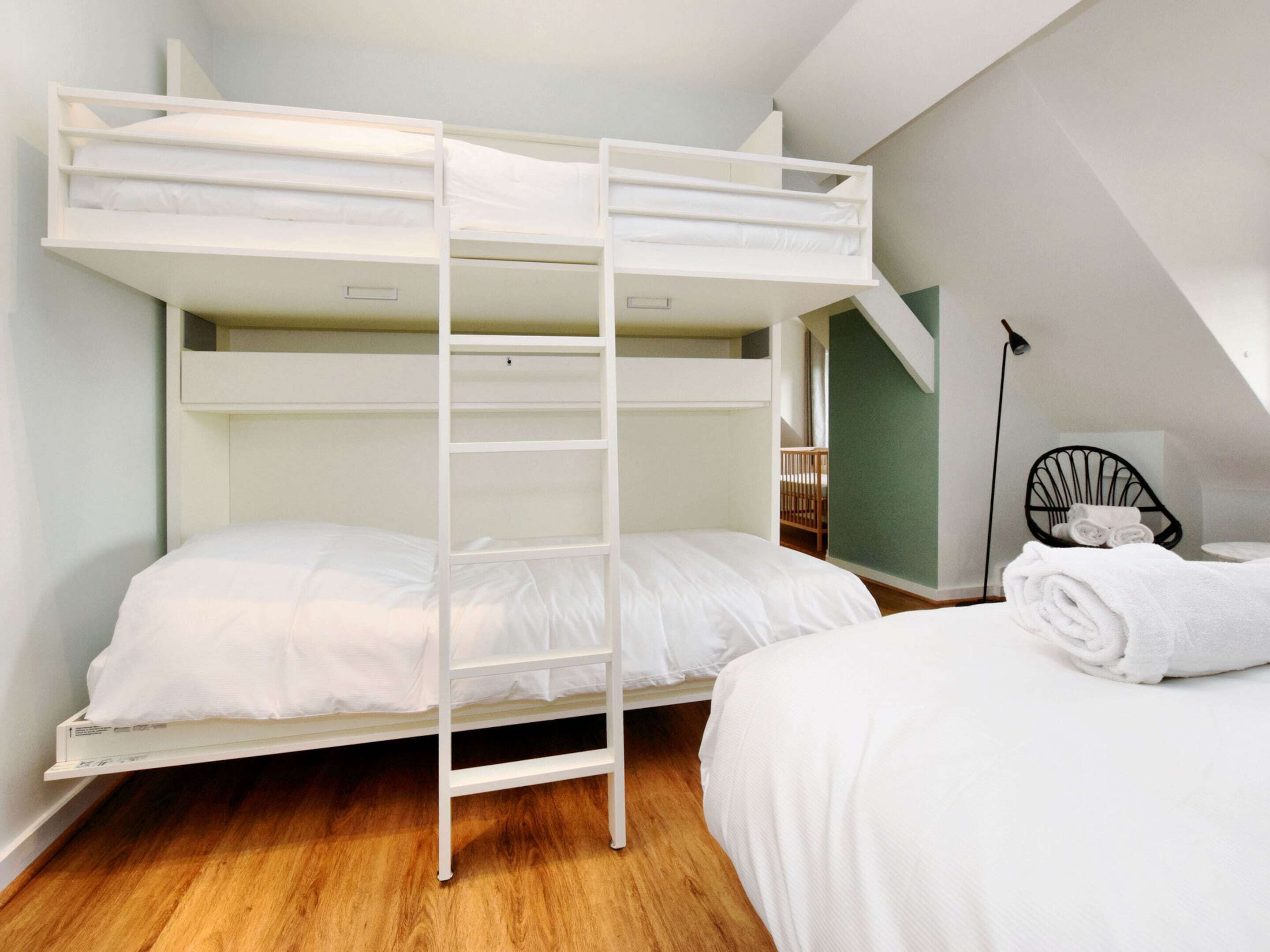 A bunk bed room with a ladder, a single bed, and a chair with towels.
