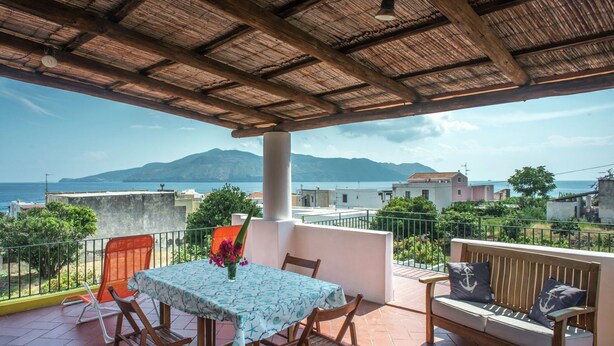 Una terraza con una mesa y sillas, un banco y vistas al mar y a las montañas.