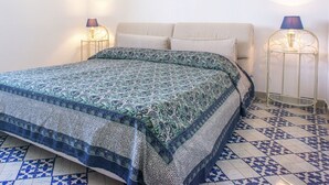 Una cama con colcha estampada, dos lámparas de noche y un adorno en la pared.