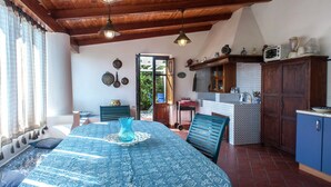 Una habitación acogedora con techo de madera, una mesa de comedor con mantel estampado en azul, y una zona de cocina con baldosas estampadas y armarios de madera.