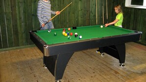 A pool table with balls and cues, a wooden floor, and a green wall. - A Grand Getaway for Family and Friends (Sysslebäck)