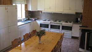 A kitchen with wooden cabinets, a stove, a refrigerator, and a dining table with chairs. - A Grand Getaway for Family and Friends (Sysslebäck)