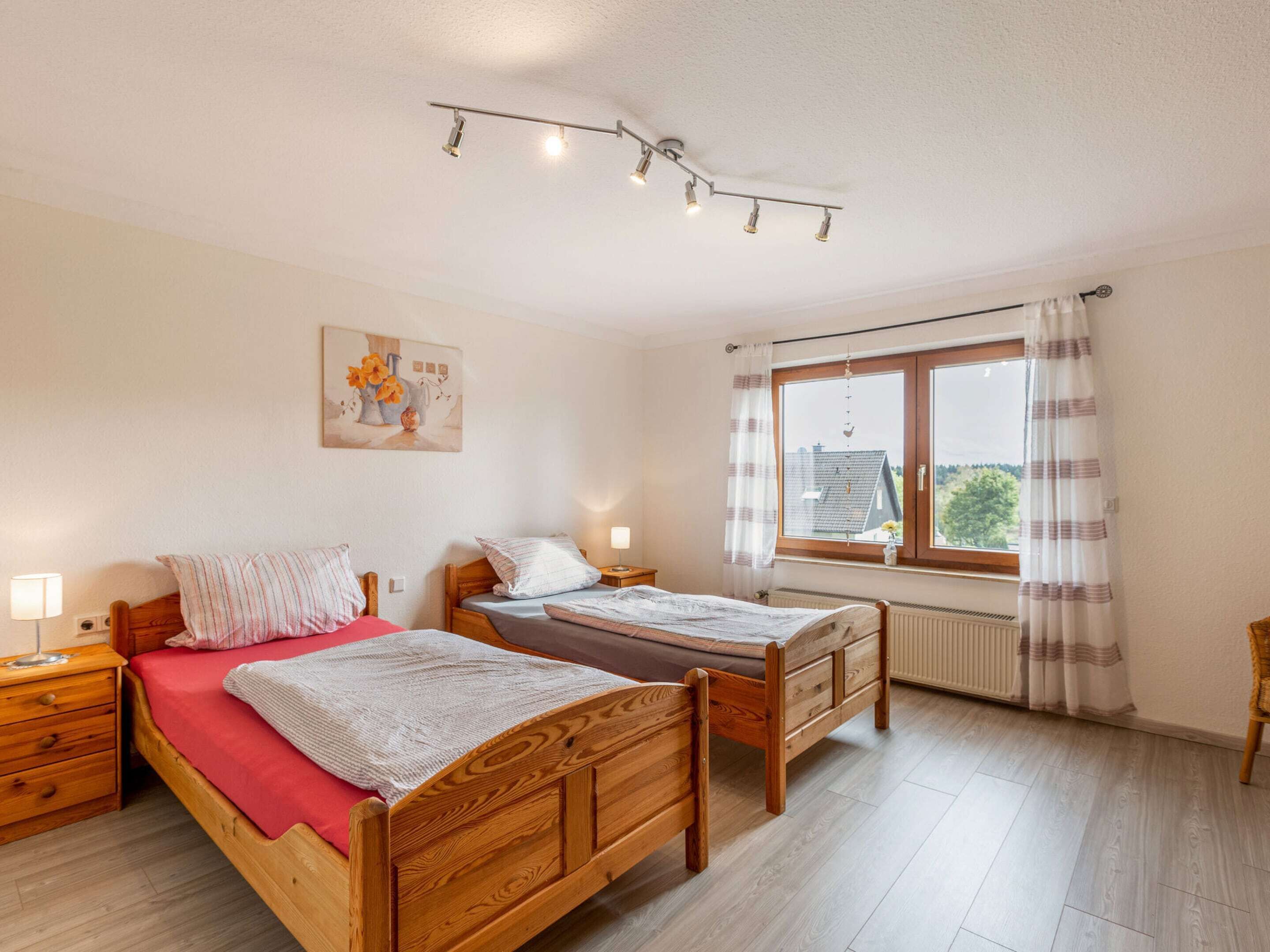 A bedroom with two wooden beds, a window with curtains, a radiator, and a painting on the wall.