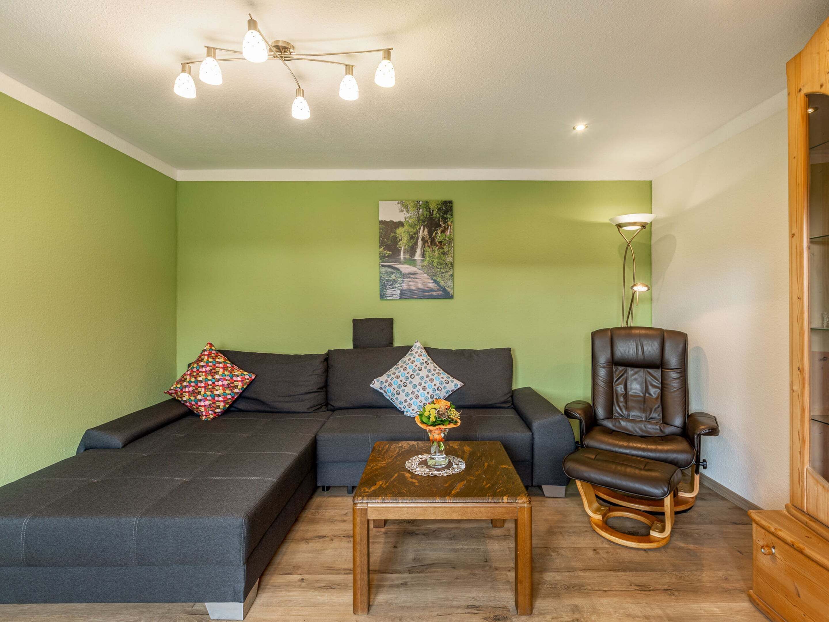 A living room with a sectional sofa, a wooden coffee table, a leather armchair, and a painting on the wall.