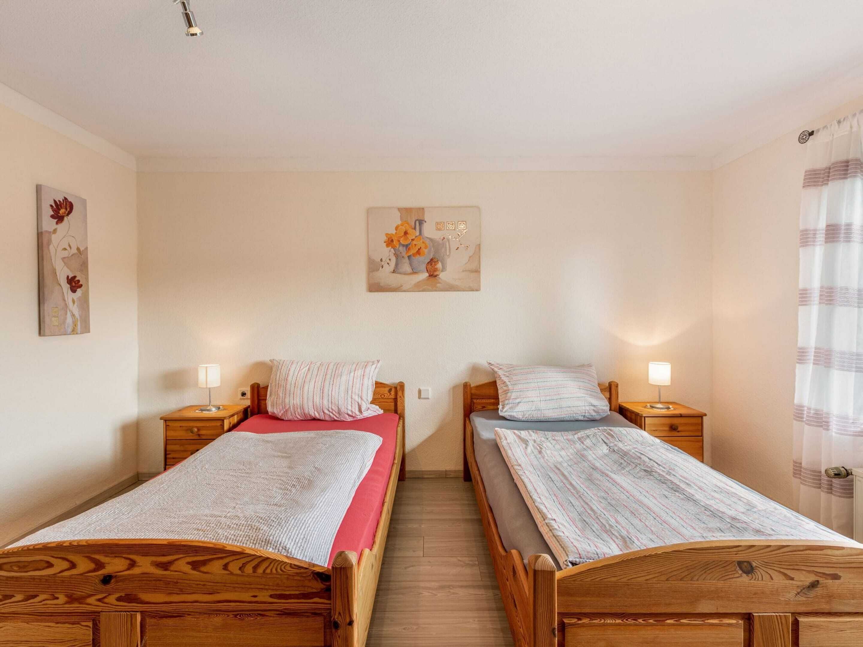 A room with two wooden beds, each with a nightstand and a lamp. There is a painting on the wall above the beds.