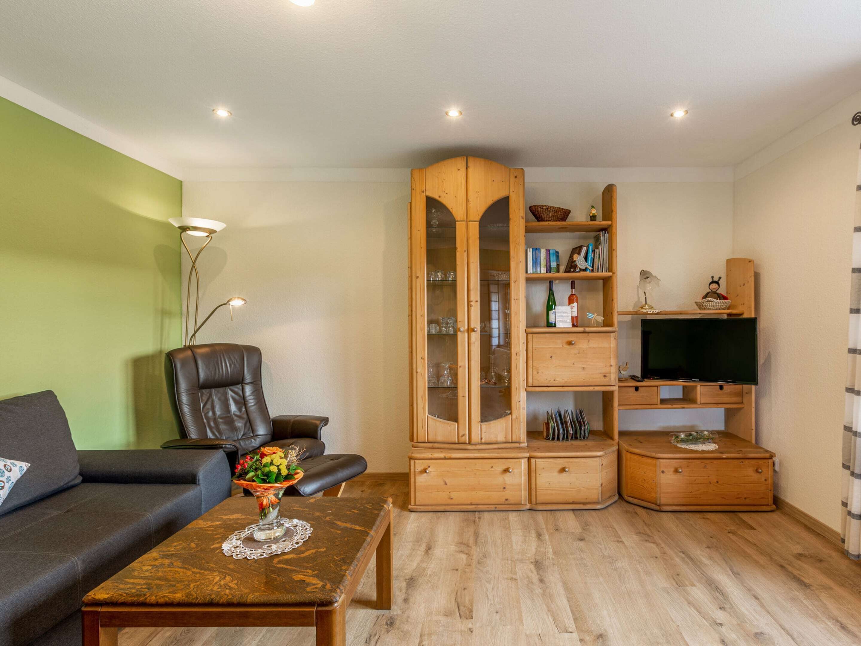A living room with a sofa, a coffee table with a vase, a wooden cabinet with glass doors, and a television.