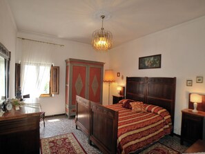 A bedroom with a wooden bed, a chandelier, a dresser, and a desk with a lamp.