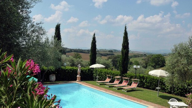 Une piscine entourée de verdure, avec des chaises longues et des parasols, et offrant une vue sur les collines.