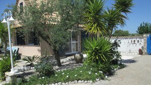 A garden with a stone wall, a palm tree, and a building with a window. - Spacious Chalet with Fruit Trees near Beach in Messinia (Messini)