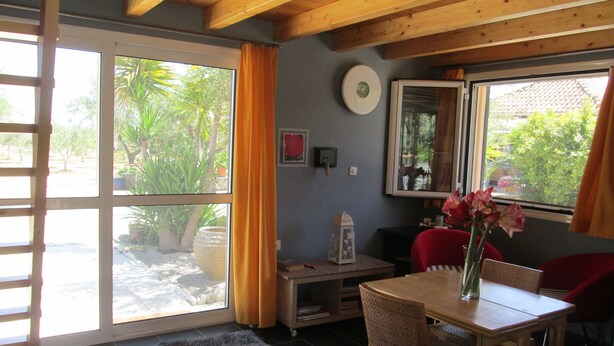 A room with a sliding glass door leading to a garden, a wooden ceiling, a small table with a vase, and a red chair. - Spacious Chalet with Fruit Trees near Beach in Messinia (Messini)