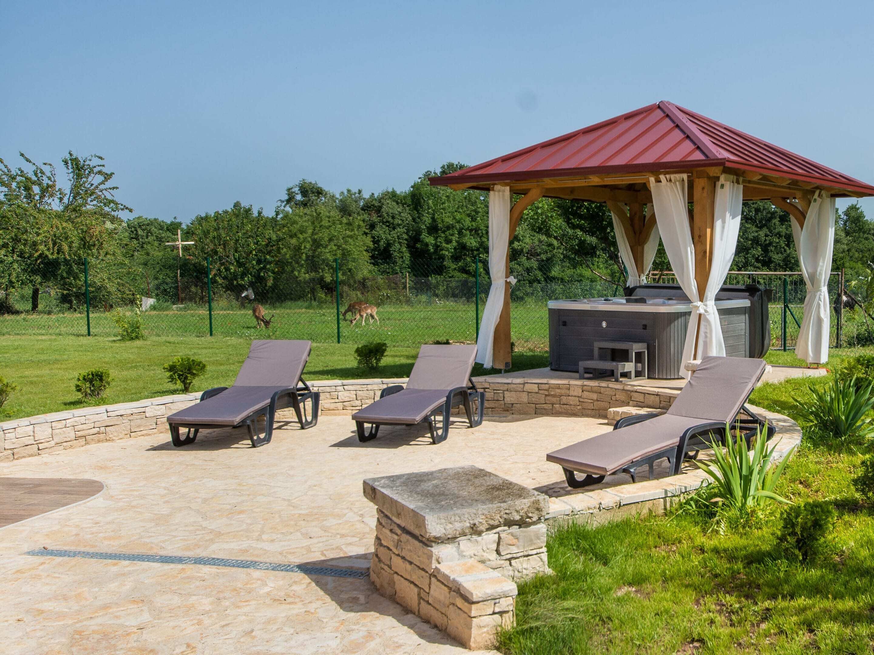 A covered outdoor seating area with lounge chairs and a hot tub.