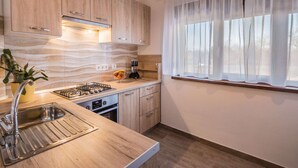 A modern kitchen with wooden cabinets, a stainless steel sink, and a window with sheer curtains. - Attractive Holiday Home with Pool, Hot Tub, Patio, Courtyard (Vodnjan)