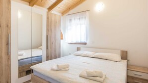 A bedroom with a wooden ceiling, a large bed with white linens and towels, a bedside table, and a window with sheer curtains. - Attractive Holiday Home with Pool, Hot Tub, Patio, Courtyard (Vodnjan)