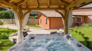 A hot tub under a wooden pergola with a stone wall and a house in the background. - Attractive Holiday Home with Pool, Hot Tub, Patio, Courtyard (Vodnjan)