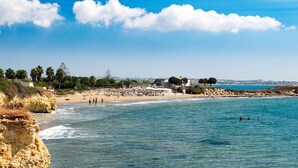 Eine Küstenlandschaft mit Strand, klarem Himmel, ruhiger See und felsigen Klippen.